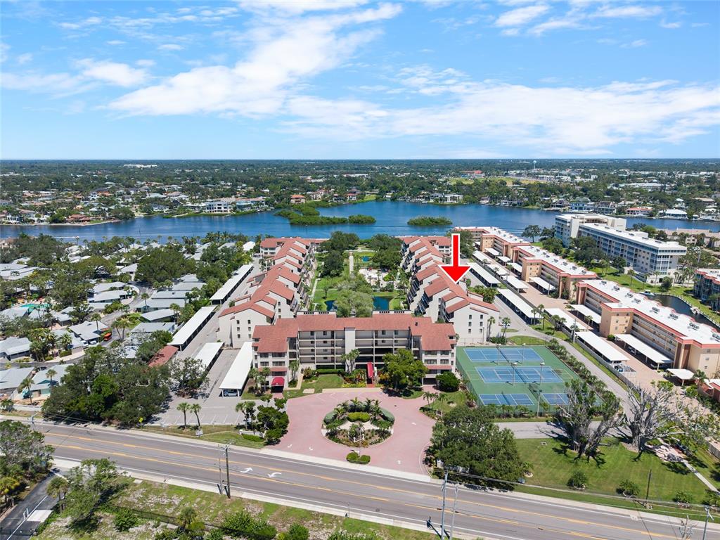An aerial view shows a multi-story apartment complex with tennis courts and a circular driveway — 6265 MIDNIGHT PASS ROAD UNIT 102, SARASOTA, FL