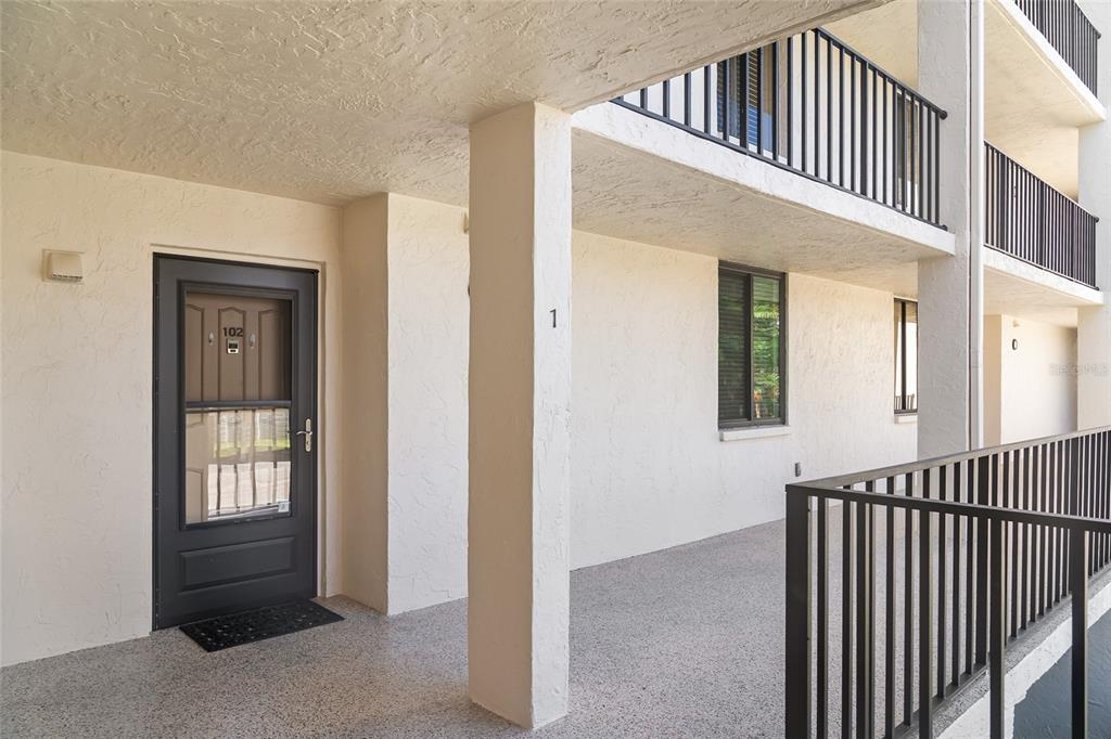 A ground-level apartment entrance features a dark grey storm door and a concrete walkway — 6265 MIDNIGHT PASS ROAD UNIT 102, SARASOTA, FL