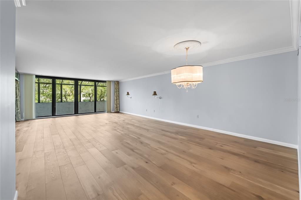 A spacious room with light wood floors, a drum chandelier, and large floor-to-ceiling windows — 6265 MIDNIGHT PASS ROAD UNIT 102, SARASOTA, FL