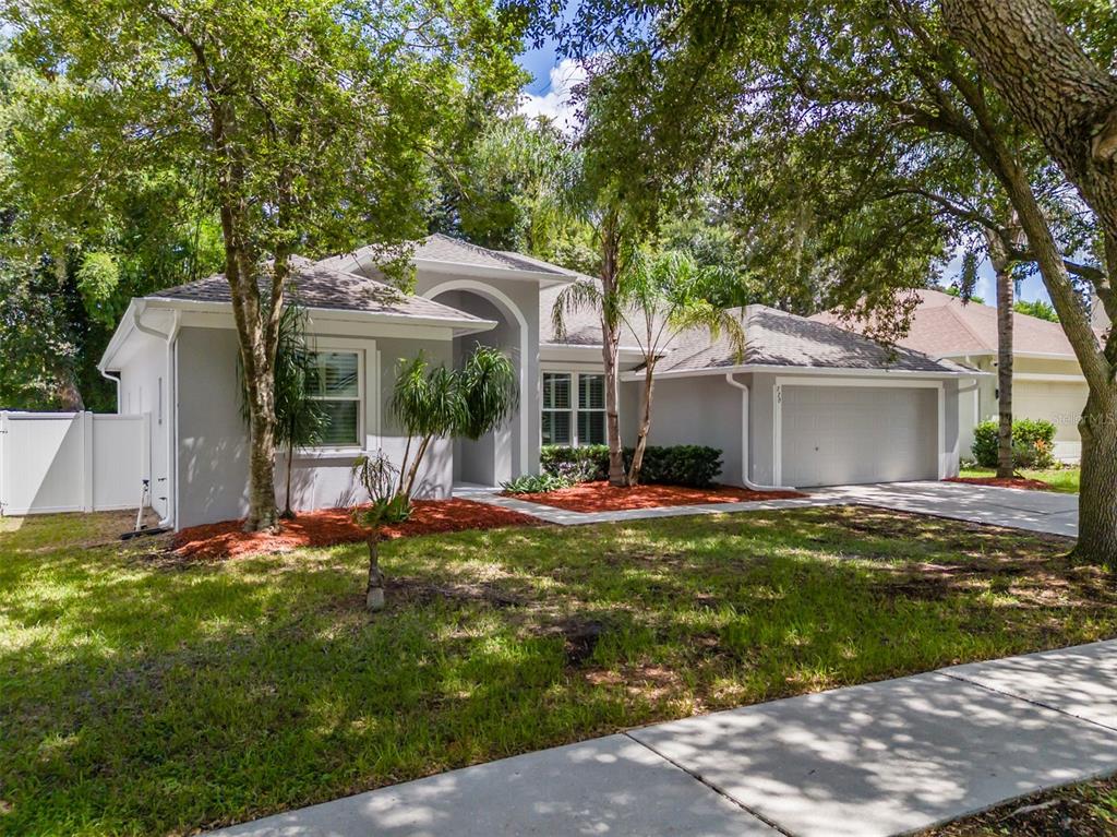 A single-story gray house with a two-car garage, arched entryway, and mature trees in front — 220 TAYLOR BAY LANE, BRANDON, FL