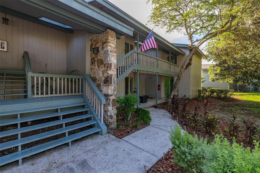An exterior walkway with a green door, potted flowers, and bicycles leads to a building entrance — 3558 CAMELOT DRIVE UNIT 3558, HAINES CITY, FL