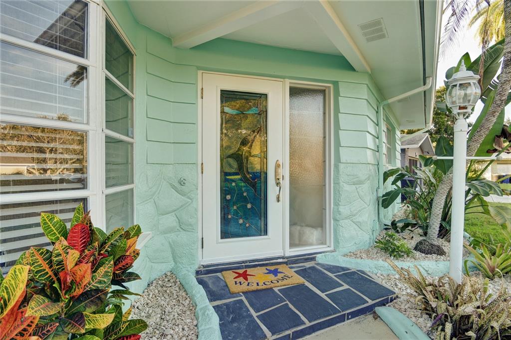A mint green house exterior features a front door with a dolphin stained glass insert — 1968 SOUVENIR DRIVE, CLEARWATER, FL