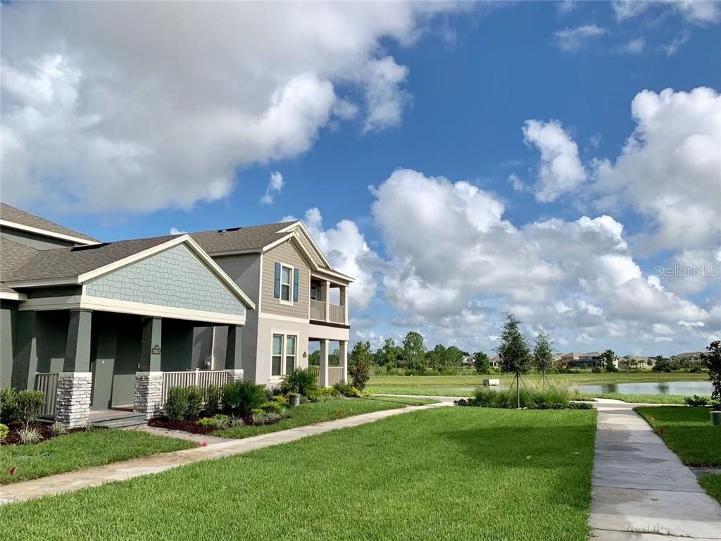 A two-story residential building with a covered porch sits beside a lawn and a pond — 10071 TAWNY MEADOW ALLEY, WINTER GARDEN, FL
