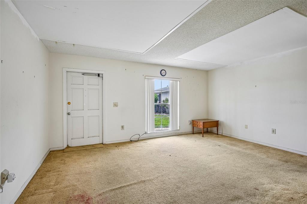 An empty room features beige carpeting, white walls, a single door, and a window — 704 RADFORD PLACE, SUN CITY CENTER, FL