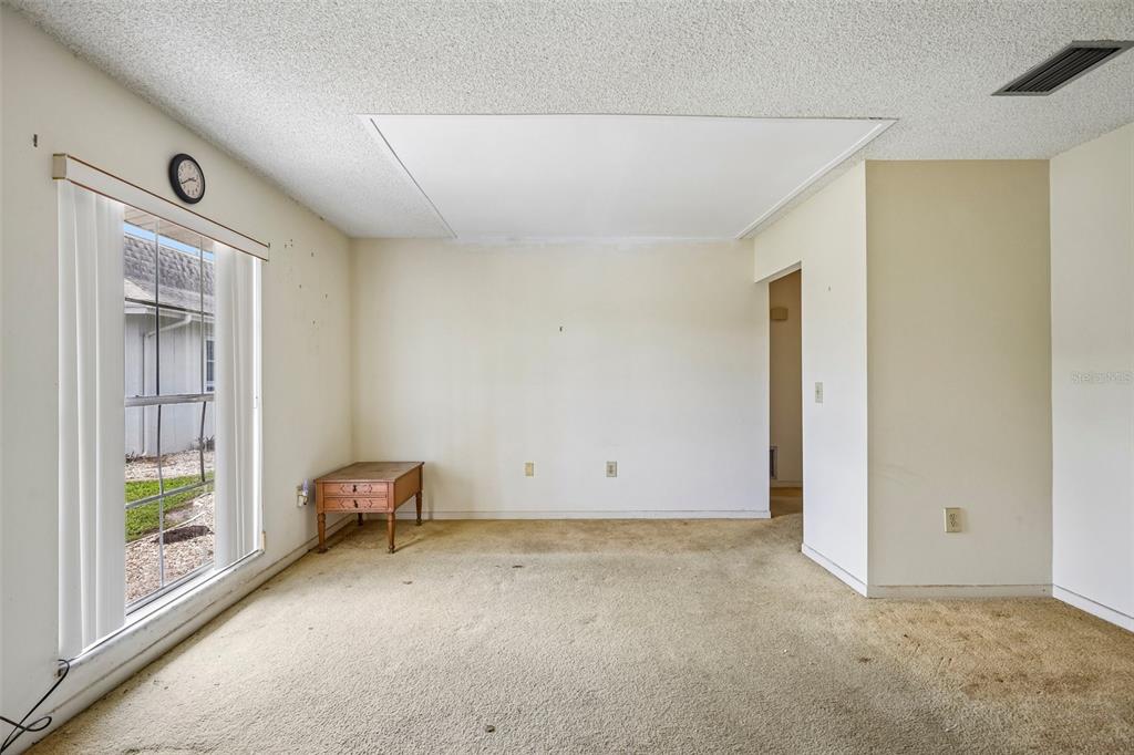An empty room with beige carpet, a large window, and a small wooden side table — 704 RADFORD PLACE, SUN CITY CENTER, FL