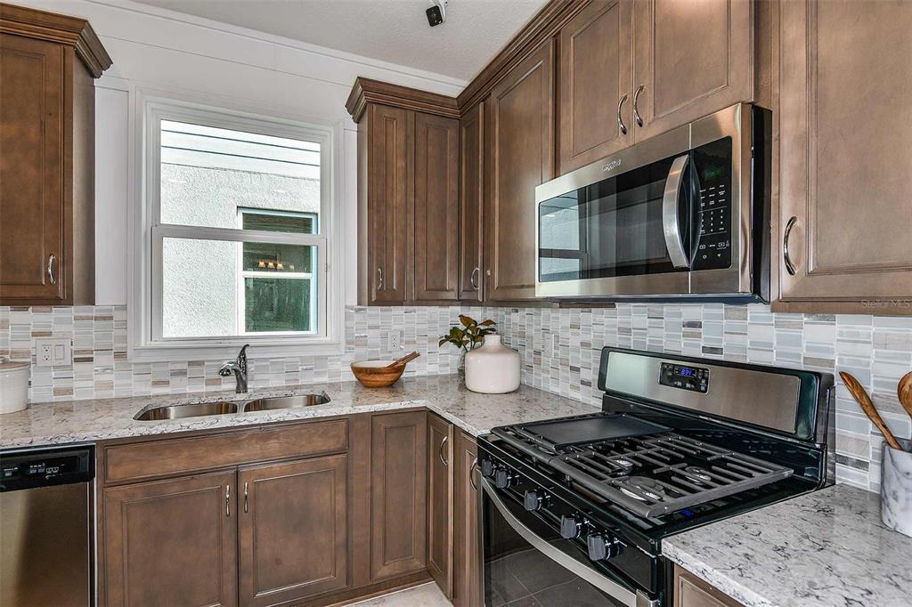 A kitchen features brown cabinets, granite countertops, a stainless steel microwave, and a gas range — 2623 HAMMOCK HARBOR AVENUE, ST CLOUD, FL