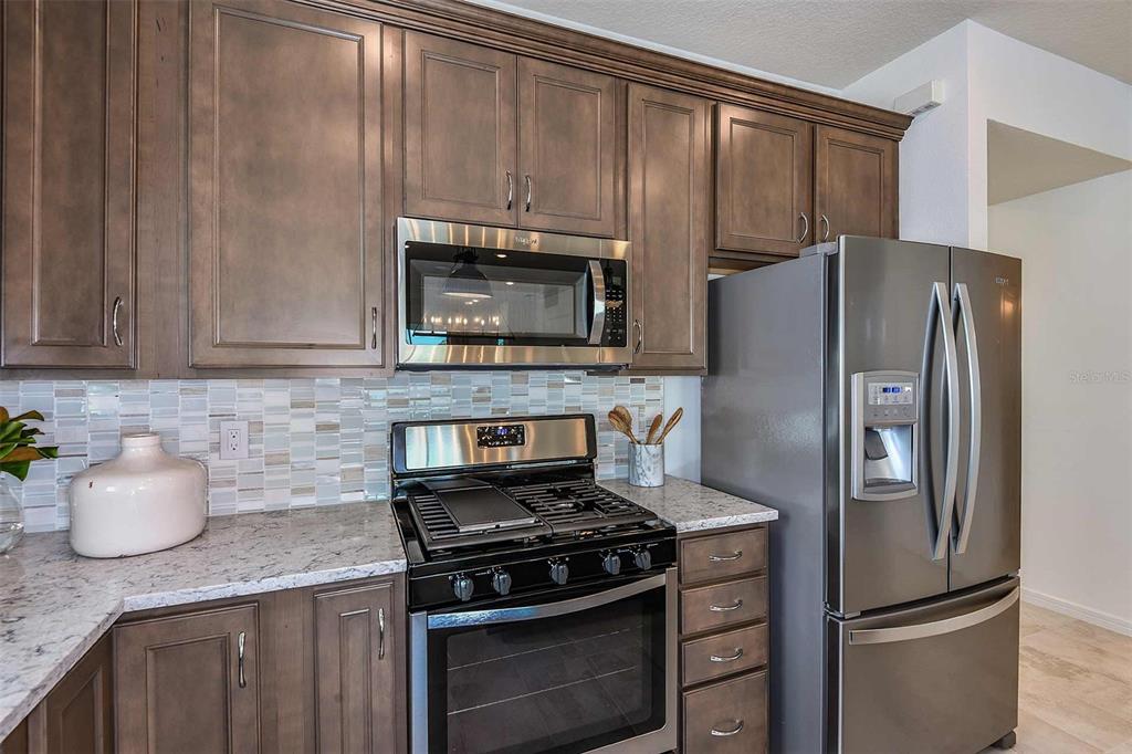 A kitchen features dark wood cabinets, stainless steel appliances, and a light-colored granite countertop — 2623 HAMMOCK HARBOR AVENUE, ST CLOUD, FL
