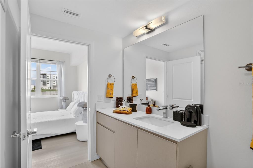 A modern bathroom features a light-colored vanity, a large mirror, and an adjacent bedroom view — 5579 MILLENIA PARK BOULEVARD UNIT 519, ORLANDO, FL