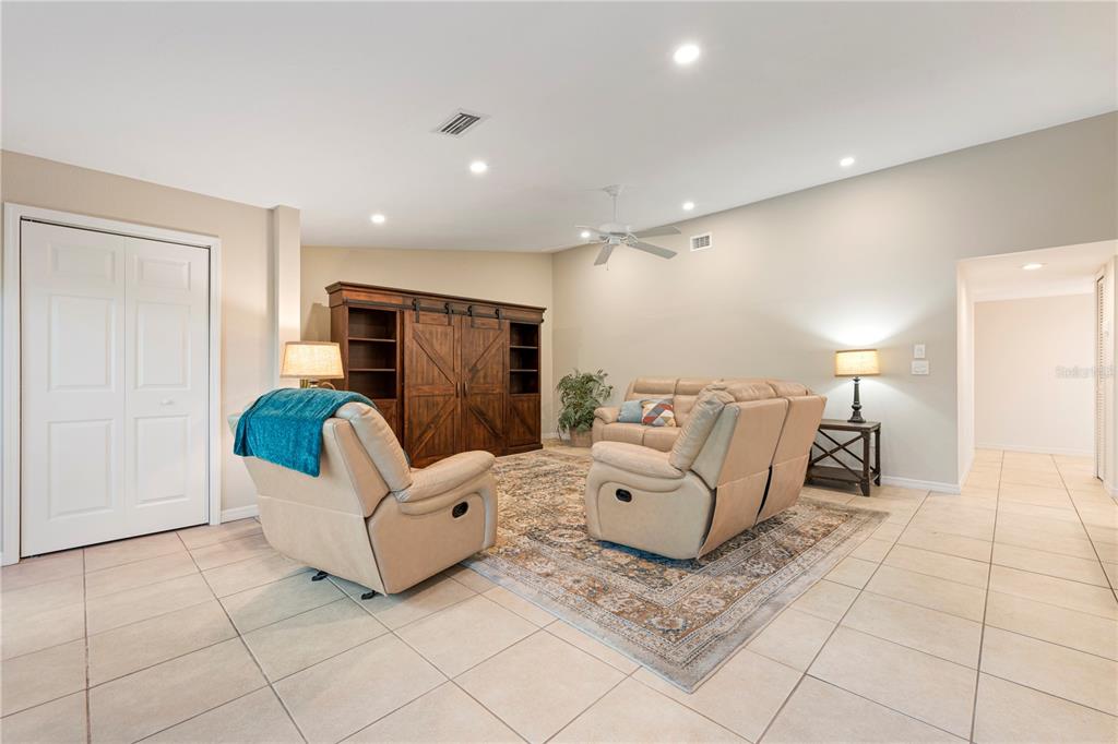 A living room features beige tile flooring, two tan reclining chairs, and a wooden entertainment center — 2756 CLUBHOUSE DRIVE UNIT 202, SARASOTA, FL