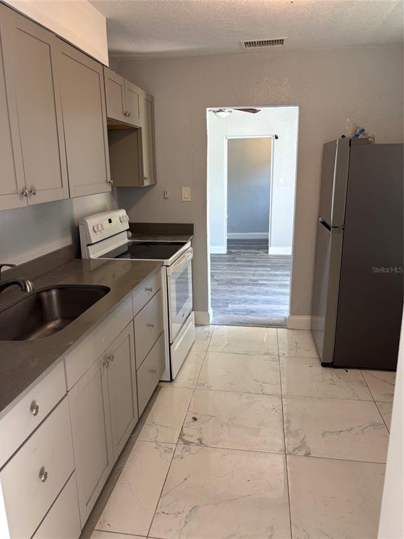 A kitchen features gray cabinets, stainless steel appliances, quartz countertops, and white marble-look tile flooring — 4321 LAKE LAWNE AVENUE, ORLANDO, FL