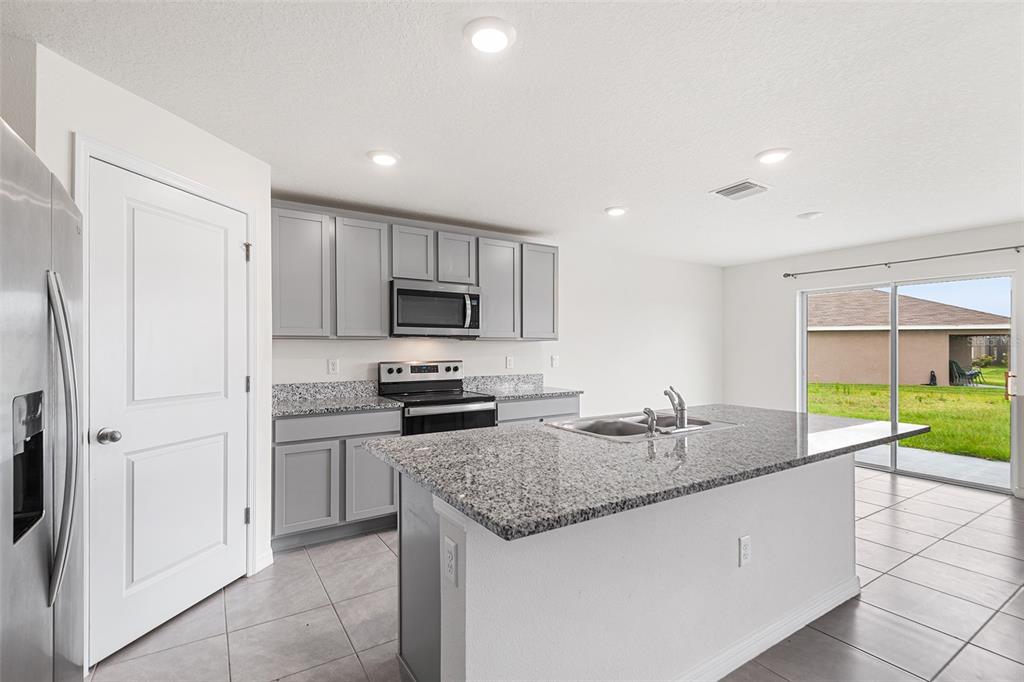A kitchen features gray cabinets, granite countertops, a center island, and a sliding glass door — 5106 PLUMERIA DRIVE, WIMAUMA, FL