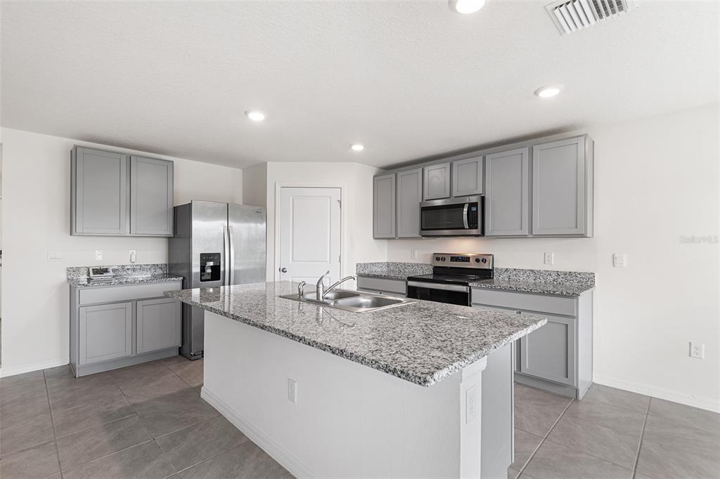 A kitchen features gray cabinets, granite countertops, stainless steel appliances, and a central island — 5106 PLUMERIA DRIVE, WIMAUMA, FL
