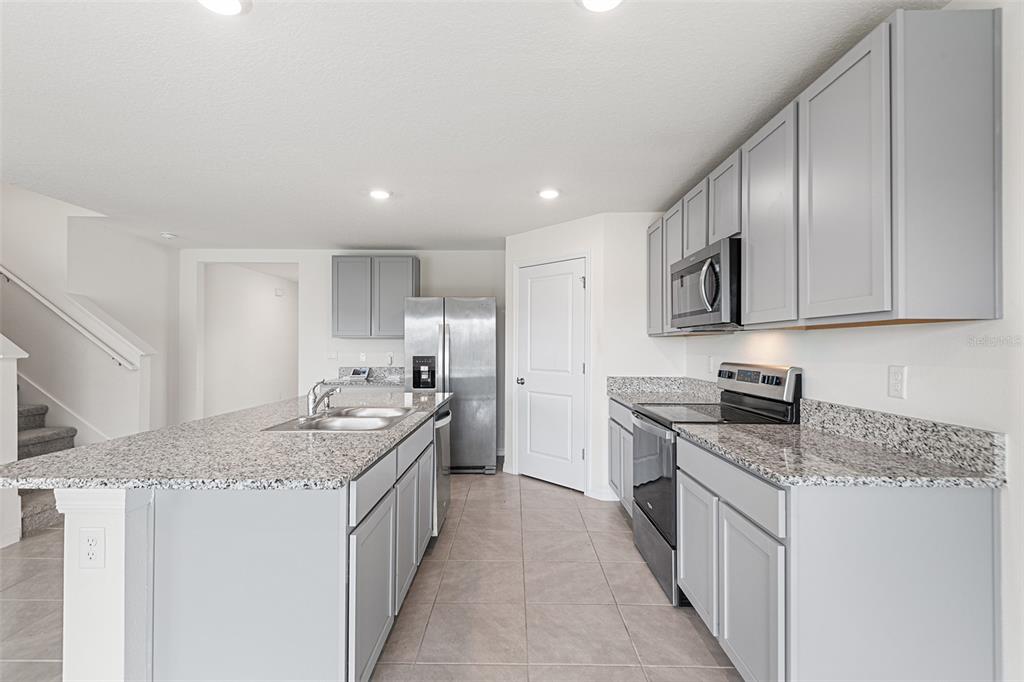 A kitchen features light gray cabinets, granite countertops, stainless steel appliances, and a central island — 5106 PLUMERIA DRIVE, WIMAUMA, FL