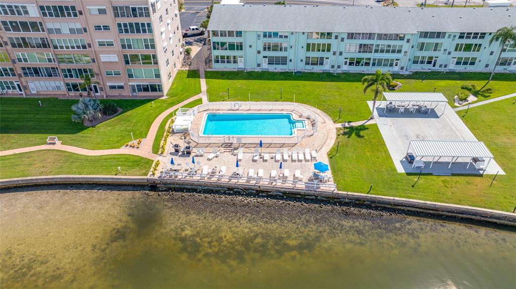 An aerial view of a swimming pool, patio area, and two apartment buildings near water — 1847 SHORE DRIVE S UNIT 509, SOUTH PASADENA, FL