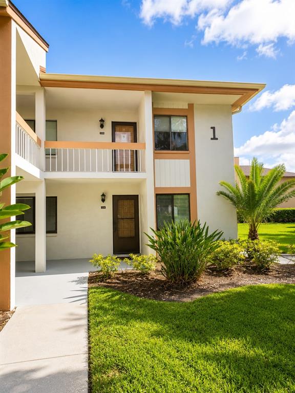 A two-story apartment building exterior features a white facade, brown trim, and a palm tree — 115 LAKEVIEW PLACE UNIT 115, OLDSMAR, FL