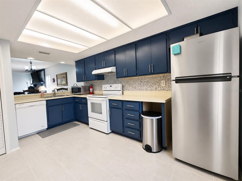 A kitchen features blue cabinets, stainless steel appliances, a white dishwasher, and a tiled backsplash — 115 LAKEVIEW PLACE UNIT 115, OLDSMAR, FL