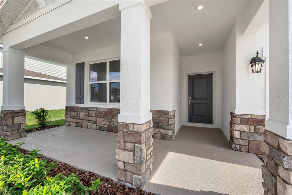 A covered front porch features stone-clad pillars, a dark front door, and a window with shutters — 9198 HARRIS HAWK DRIVE, LEESBURG, FL