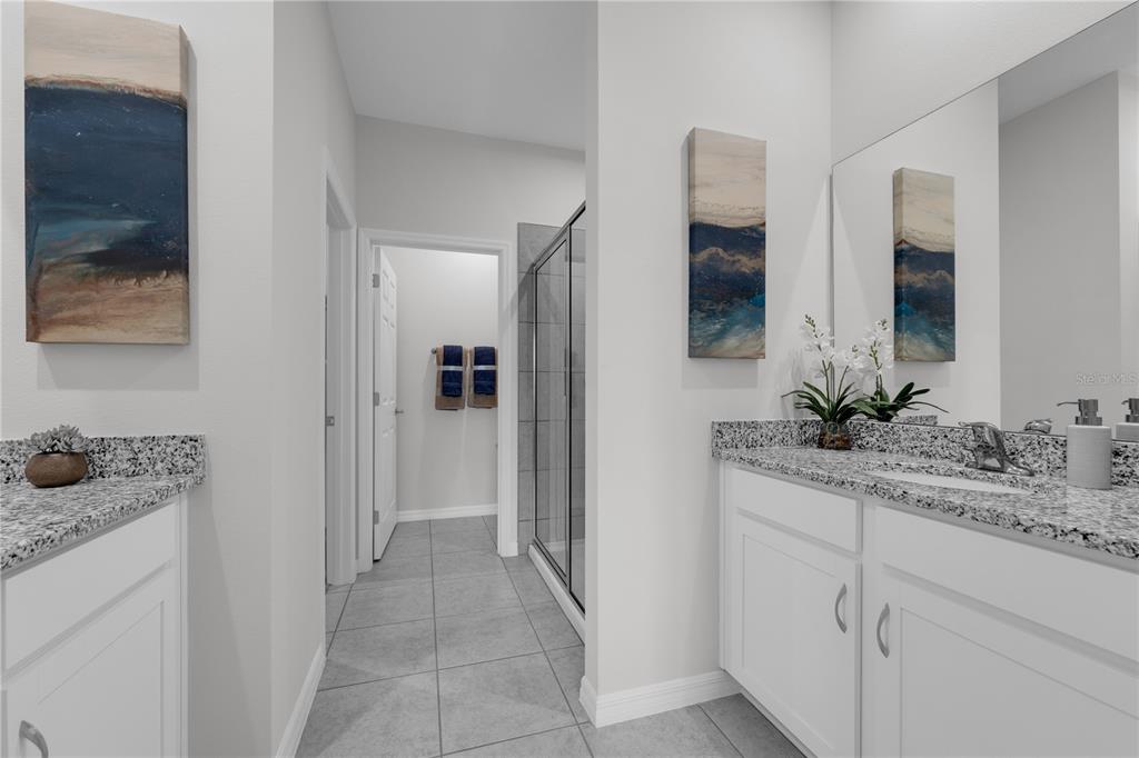 A bathroom features dual white vanities with granite countertops, a walk-in shower, and tile flooring — 9198 HARRIS HAWK DRIVE, LEESBURG, FL