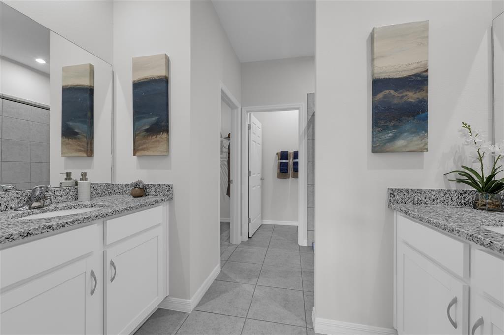 A bathroom with dual white vanities, granite countertops, tile flooring, and two framed abstract paintings — 9198 HARRIS HAWK DRIVE, LEESBURG, FL