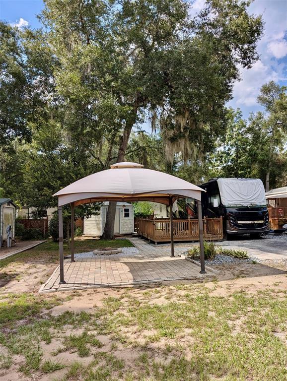 A tan gazebo stands on a paved patio next to a wooden deck and an RV — 25105 NE 143RD STREET, SALT SPRINGS, FL