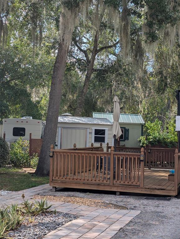 A wooden deck with a patio umbrella sits in front of a trailer and small shed — 25105 NE 143RD STREET, SALT SPRINGS, FL