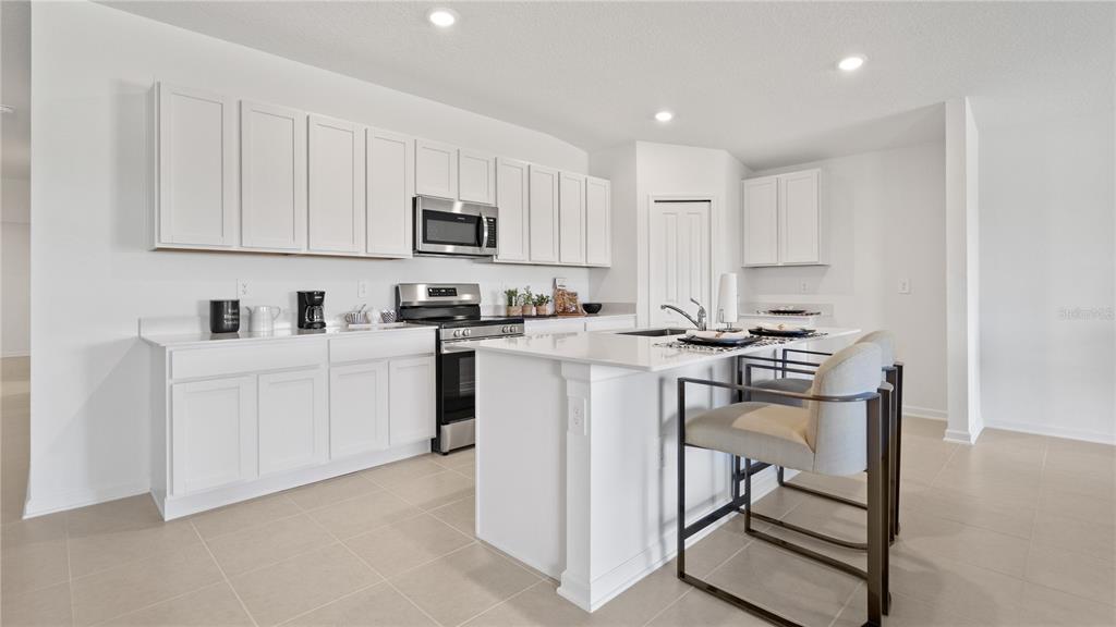 A modern kitchen features white cabinetry, quartz countertops, a center island, and stainless steel appliances — 1940 PINE MEADOWS GOLFCOURSE ROAD, EUSTIS, FL