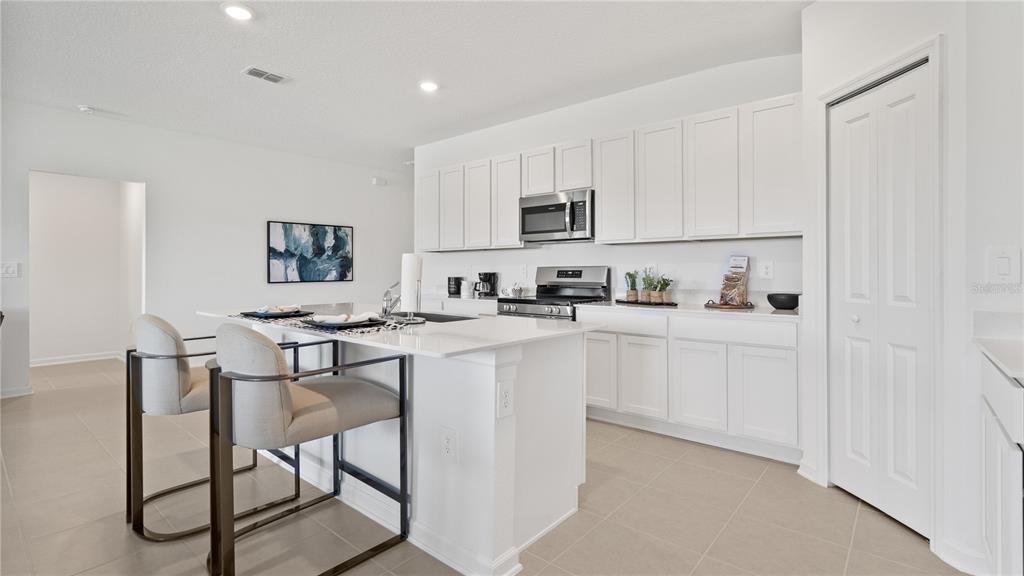 A modern kitchen features white cabinetry, a central island with bar seating, and tile flooring — 1940 PINE MEADOWS GOLFCOURSE ROAD, EUSTIS, FL