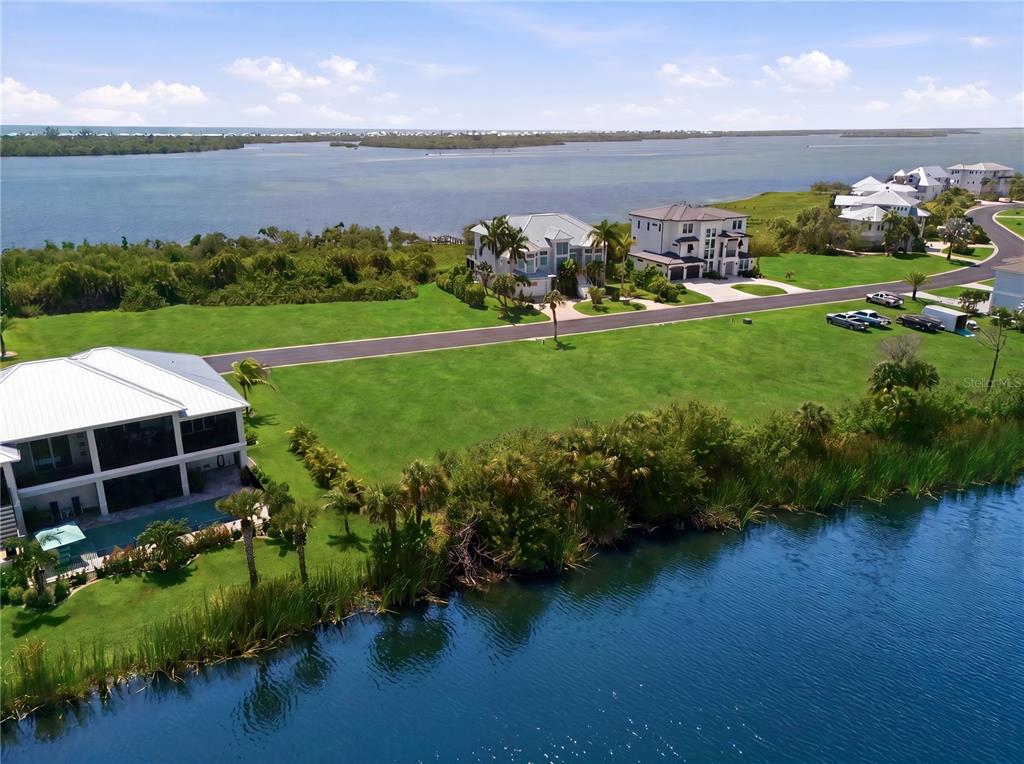 An aerial view shows waterfront homes, a large grassy lot, and a road near water — 10000 EAGLE PRESERVE DRIVE, ENGLEWOOD, FL