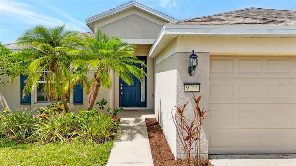 The exterior of a house features a tan garage, a blue front door, and palm trees — 9784 50TH STREET CIRCLE E, PARRISH, FL