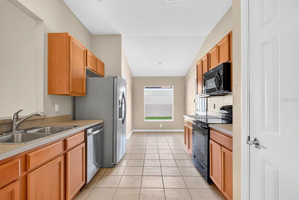 A galley-style kitchen features wood cabinets, stainless steel appliances, and beige tile flooring — 9784 50TH STREET CIRCLE E, PARRISH, FL