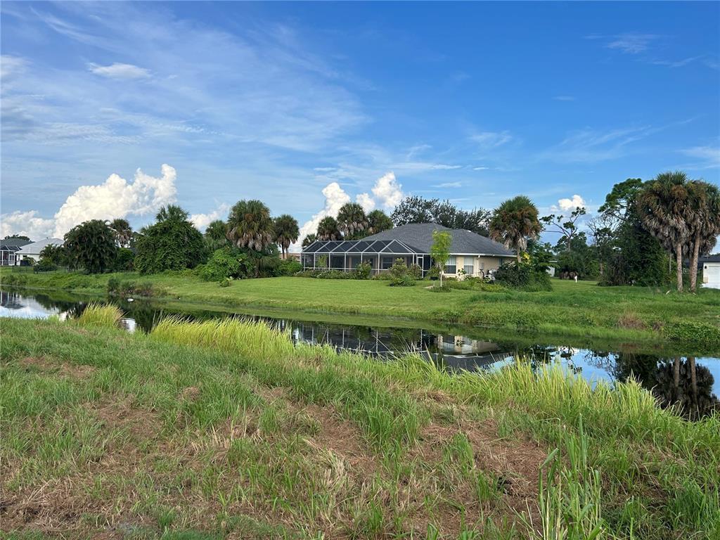 A house with a screened-in lanai sits behind a grassy bank and a small canal — 105 MARKER ROAD, ROTONDA WEST, FL