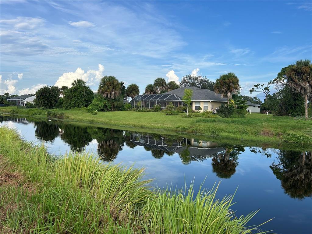A house with a screened-in pool enclosure sits behind a canal with grassy banks — 105 MARKER ROAD, ROTONDA WEST, FL