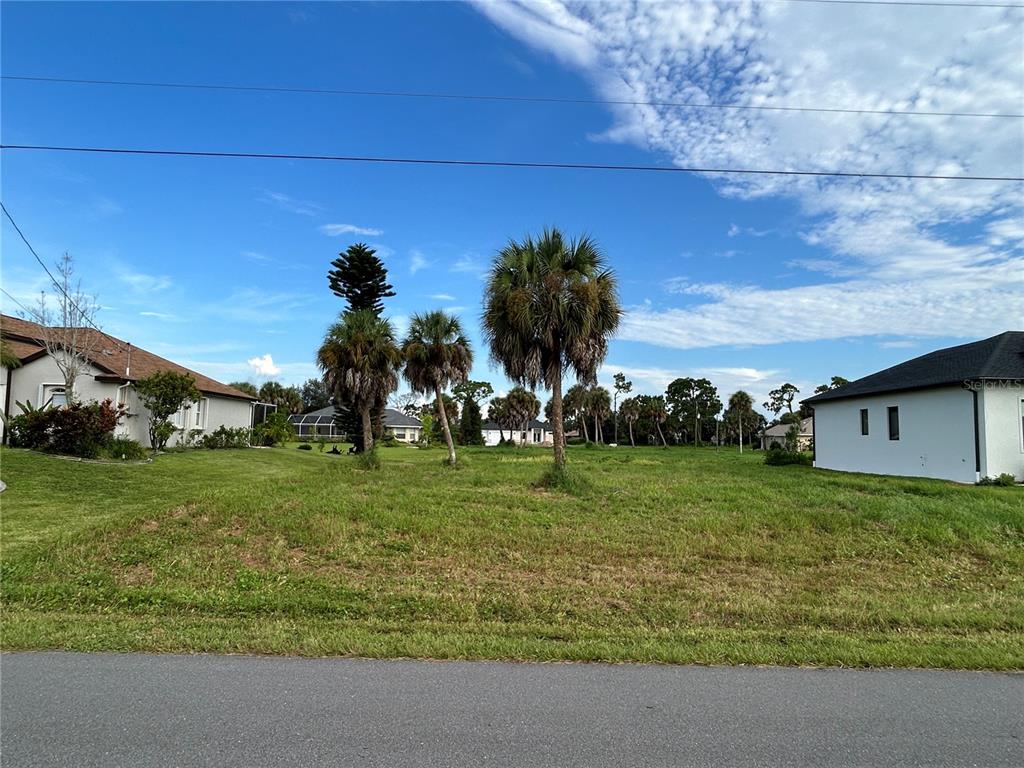 A vacant grassy lot sits between two residential houses under a bright blue sky — 105 MARKER ROAD, ROTONDA WEST, FL