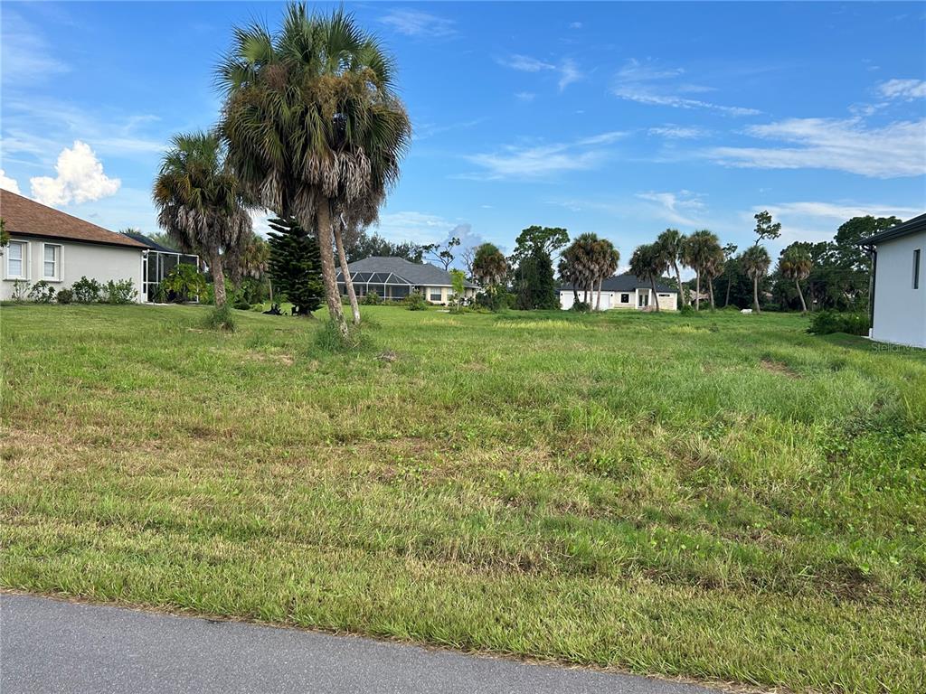 A grassy vacant lot sits between residential houses under a blue sky with palm trees — 105 MARKER ROAD, ROTONDA WEST, FL