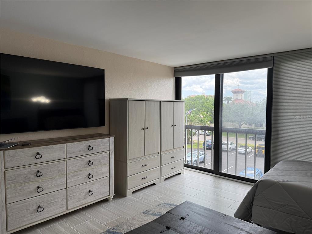 A bedroom features a large television, light wood furniture, tile flooring, and a balcony view — 255 DOLPHIN POINT UNIT 305, CLEARWATER BEACH, FL