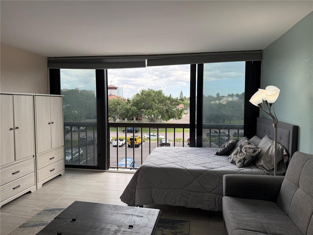 A bedroom with a bed, sofa, wardrobe, and sliding glass doors overlooking a parking lot — 255 DOLPHIN POINT UNIT 305, CLEARWATER BEACH, FL