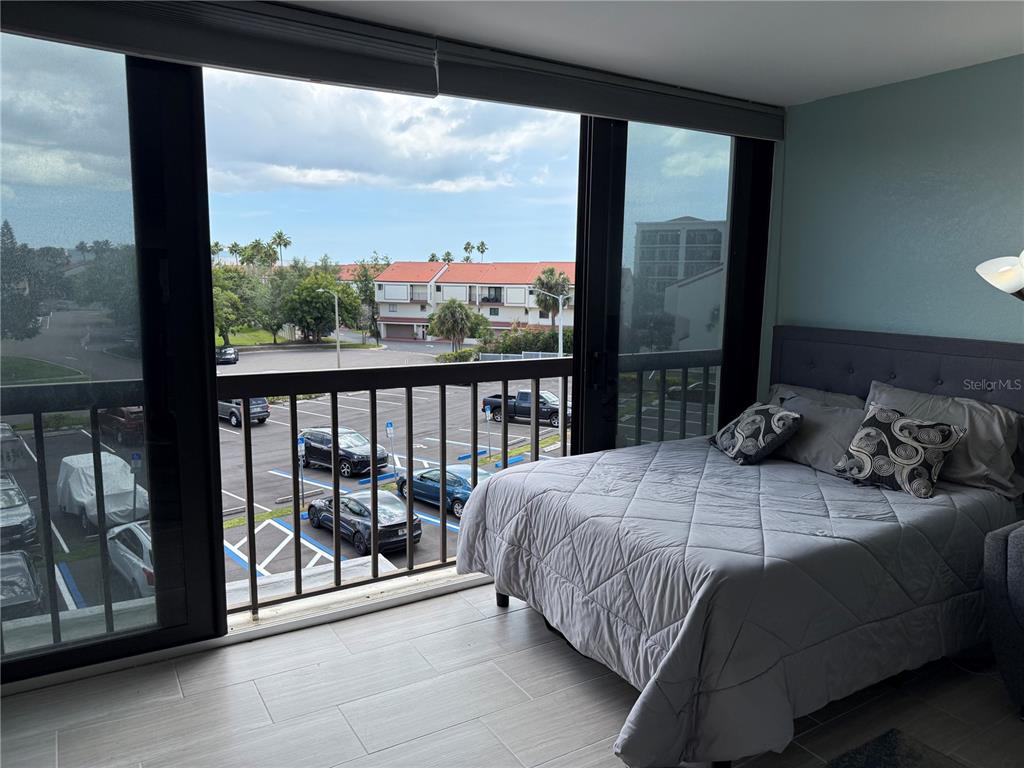A bedroom with a gray bed and a sliding glass door opening to a balcony — 255 DOLPHIN POINT UNIT 305, CLEARWATER BEACH, FL