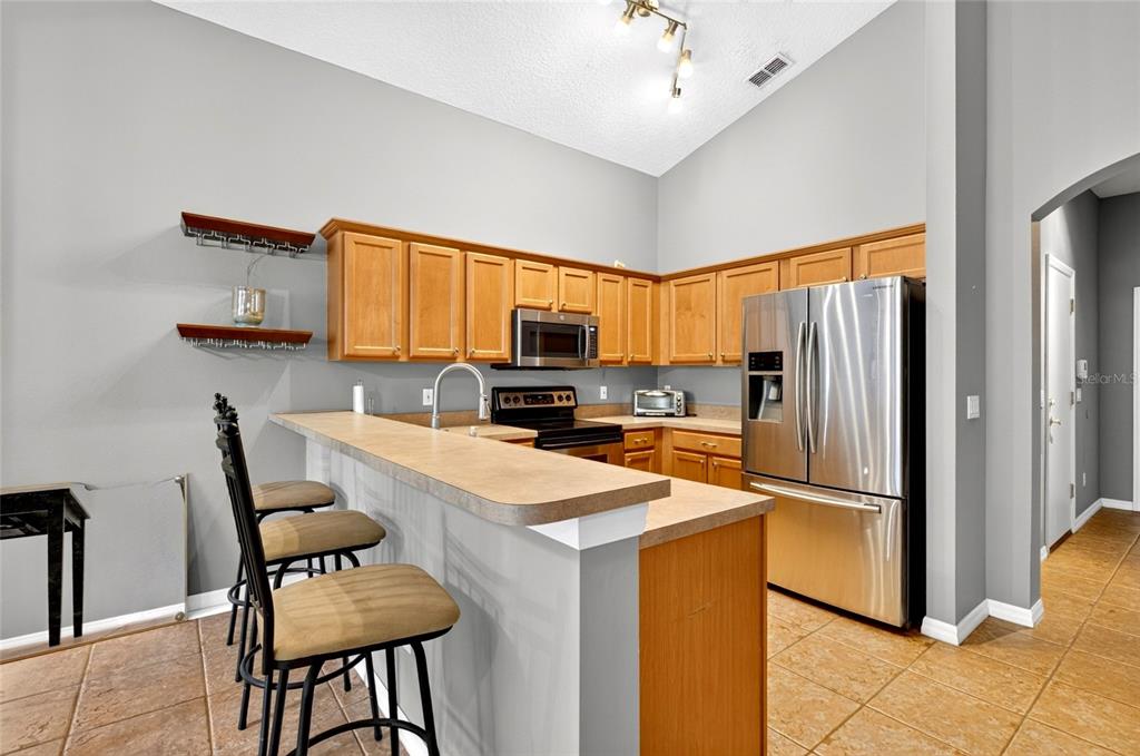A kitchen features light wood cabinets, stainless steel appliances, a breakfast bar, and tile flooring — 4618 CONROY CLUB DRIVE, ORLANDO, FL
