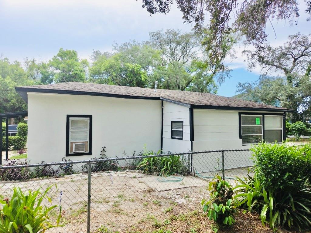 A side view of a single-story house with white stucco and siding behind a chain-link fence — 1018 E HOLLAND AVENUE, TAMPA, FL