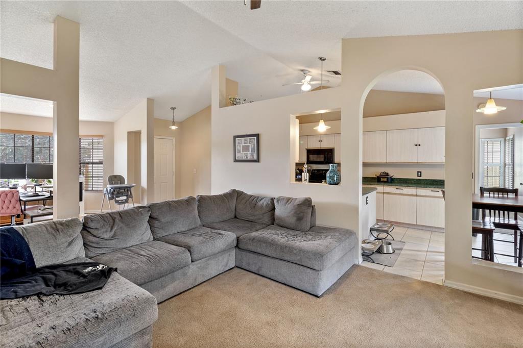 A living room with a gray sectional sofa opens to a kitchen through a pass-through window — 1921 SW GRANELLO TERRACE, PORT ST LUCIE, FL