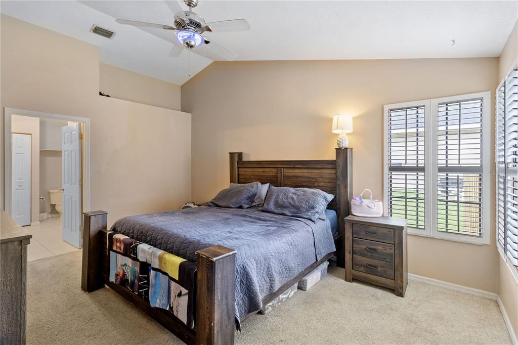 A bedroom features a wooden bed frame, a ceiling fan, and a window with shutters — 1921 SW GRANELLO TERRACE, PORT ST LUCIE, FL