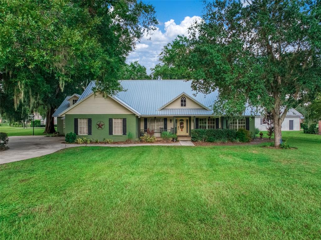 A covered front porch features a red hanging bench, two rocking chairs, and brick flooring — 510 EDGEWOOD DRIVE, FORT MEADE, FL
