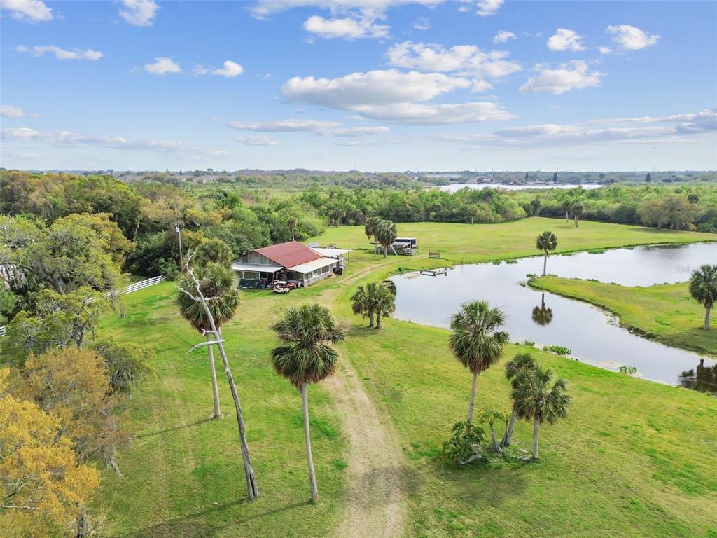 An aerial view of a rural property featuring a barn, pond, and scattered palm trees — KIBLER LN, HOLIDAY, FL