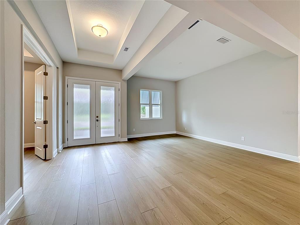 An empty room with light wood flooring, a tray ceiling, and double glass doors — 12422 STONEGATE TRAIL, PARRISH, FL