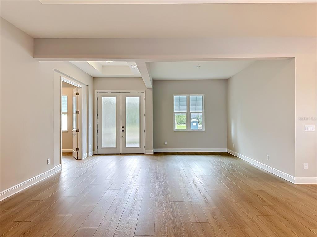 An empty room features light wood flooring, neutral walls, a double door, and a window — 12422 STONEGATE TRAIL, PARRISH, FL
