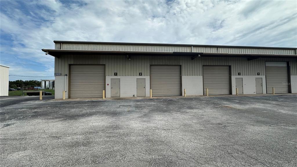 A commercial warehouse building features multiple roll-up doors and pedestrian entrances along a paved lot — 3120-3126 REYNOLDS ROAD, LAKELAND, FL