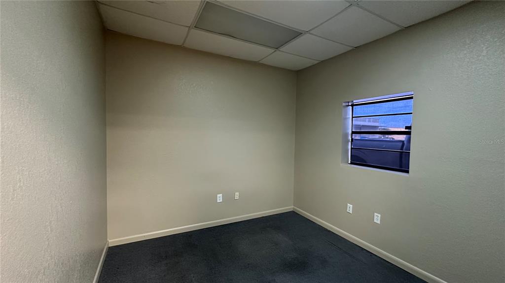An empty office with beige walls, gray carpet, a drop ceiling, and a small window — 3120-3126 REYNOLDS ROAD, LAKELAND, FL