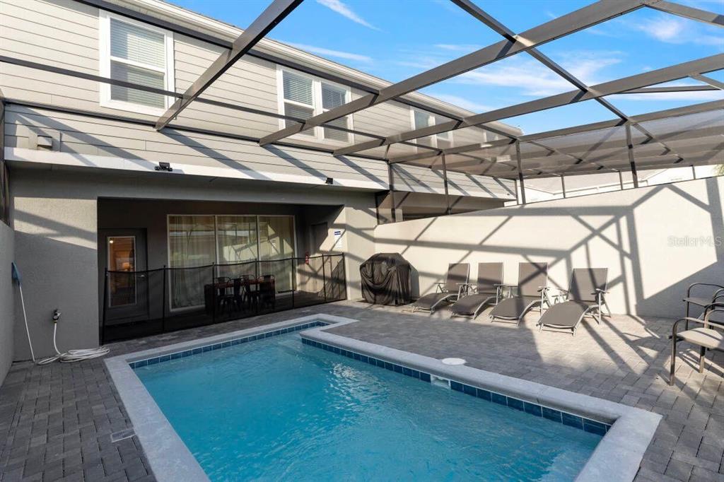 A screened-in patio features a rectangular swimming pool, lounge chairs, and a grill — 7108 OAKMOSS LOOP, DAVENPORT, FL