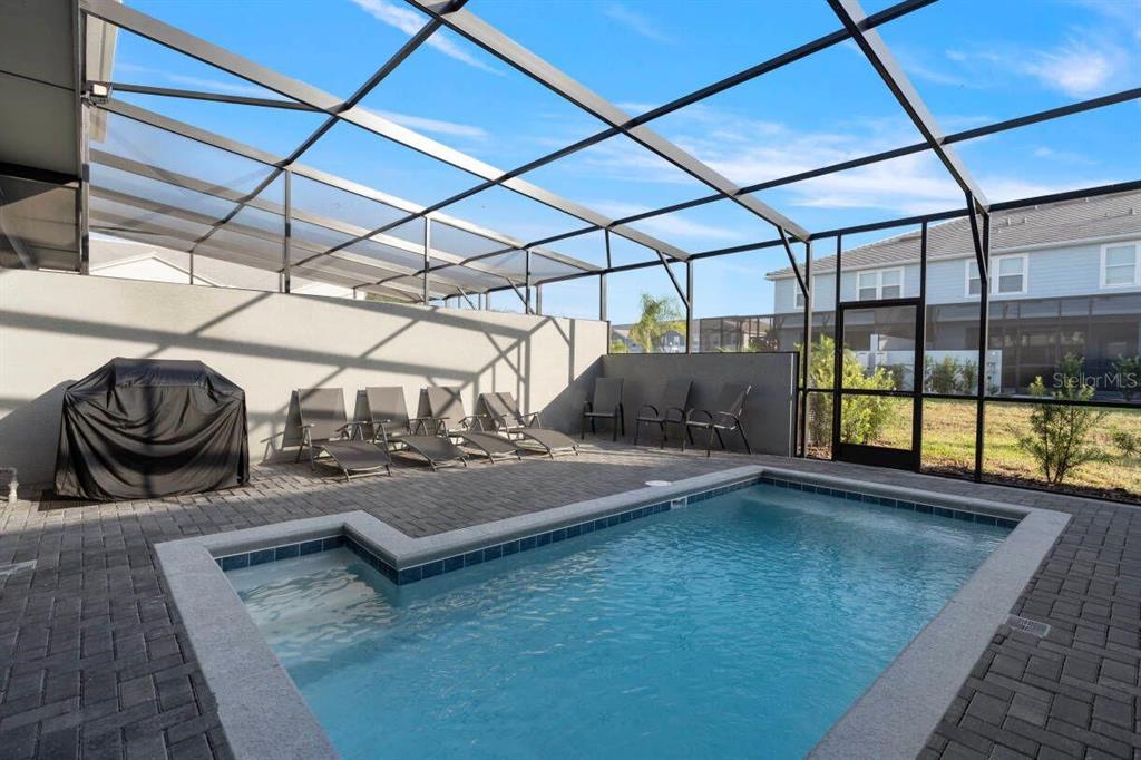 A screened-in patio features a rectangular swimming pool, lounge chairs, and a covered grill — 7108 OAKMOSS LOOP, DAVENPORT, FL