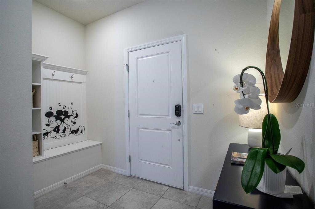 An entryway features a white door, a built-in bench with Mickey Mouse decals, and tile flooring — 7108 OAKMOSS LOOP, DAVENPORT, FL